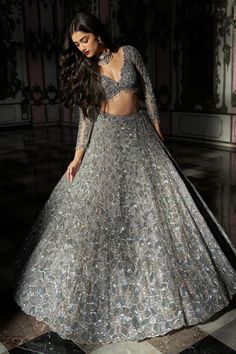 a woman in a silver gown with long sleeves and a cutout top is standing on the floor