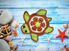 a crocheted turtle is surrounded by seashells and starfish on a blue wooden surface