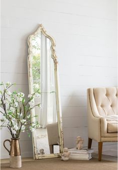 a large white mirror sitting on top of a floor next to a chair and vase