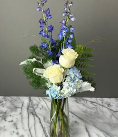 a vase filled with blue and white flowers on top of a marble counter next to a gray wall