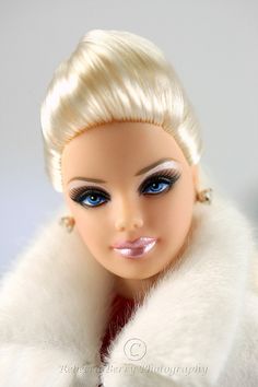 a doll with blonde hair and blue eyes wearing a white fur stole around her neck