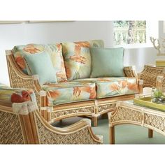 a living room with wicker furniture and tropical print pillows on the couch, coffee table and side tables