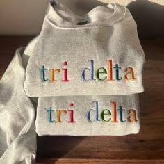 a white shirt with the words tri delta and tri delta on it sitting on top of a wooden table