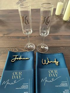 two wine glasses sitting next to each other on top of a blue napkin with gold lettering