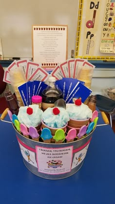 a bucket filled with lots of cupcakes sitting on top of a blue table