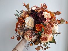 a woman holding a bouquet of flowers in her hand with leaves on it and an orange flower