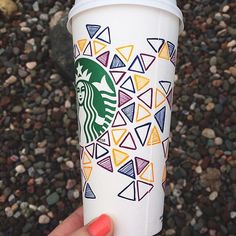 a starbucks cup with colorful designs on it is being held by a woman's hand