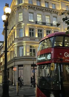 a red double decker bus driving down a street next to tall buildings and traffic lights