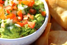 a white bowl filled with guacamole surrounded by tortilla chips and salsa