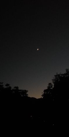 the moon is shining brightly in the dark night sky over some trees and hills with no leaves on them