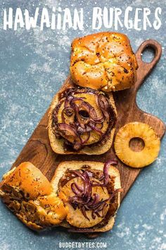 three hawaiian burgers on a wooden cutting board with pineapple slices and onion rings