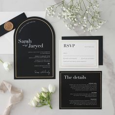 the black and gold wedding suite is laid out on top of a marble table with white flowers