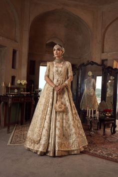 a woman standing in front of a mirror wearing a wedding dress with gold embroidery on it