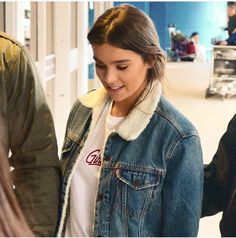 a woman in a denim jacket is looking at her cell phone while walking through an airport