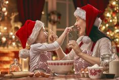 two women dressed in santa hats are eating food at a table with christmas decorations on the wall behind them