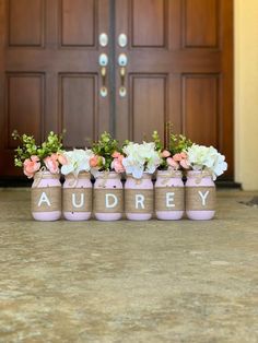 four jars with flowers in them are sitting on the floor next to a front door