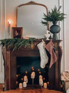 a mantel with candles and stockings on it in front of a mirror, decorated with greenery