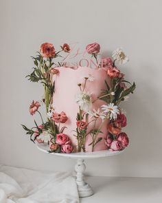 a pink cake decorated with flowers and the word love on it is sitting on a white pedestal