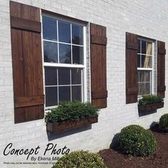 three windows with wooden shutters on the side of a white brick building and green bushes in front