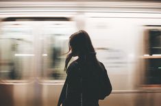 a woman standing in front of a train at a station with her back to the camera