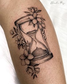 a tattoo with an hourglass and flowers on the thigh, it is black and white