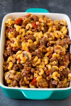 a blue casserole dish filled with pasta and ground beef, topped with tomato sauce