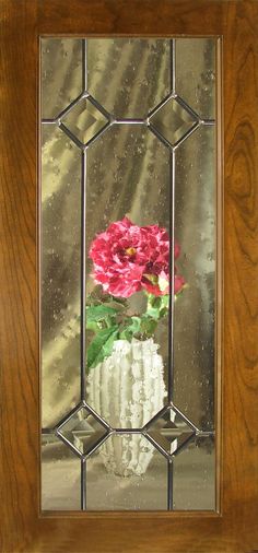 a vase with flowers in it is reflected in a glass wall mirror on a wooden frame