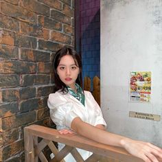 a woman standing on a wooden bench in front of a brick wall with her arms crossed