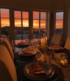 a dining room table with plates and candles on it at dusk, overlooking the ocean