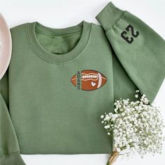 a green sweatshirt with a football embroidered on the front, and white flowers next to it