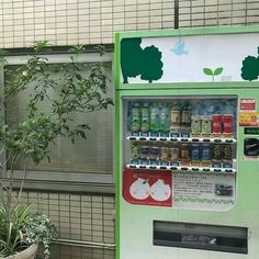 a vending machine sitting in front of a building next to a tree and potted plant