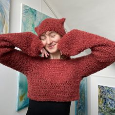 a woman wearing a red knitted sweater is smiling and holding her hands behind her head