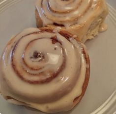 two cinnamon rolls on a plate with icing