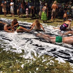 several people are laying on the ground covered in foam and water while others look on