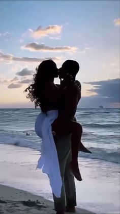 a man holding a woman on the beach at sunset