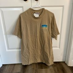 Ron Jon Surf Shop Tan Graphic Shirt Size L In Good Used Condition Brand New With Tags Summer Graphic Tee Shirt In Brown, Khaki Graphic Print Short Sleeve Tops, Brown Summer Graphic Tee Shirt, Summer Khaki Crew Neck Shirt, Summer Brown Graphic Tee Shirt, Casual Beige Graphic Print Shirt, Casual Beige Shirt With Graphic Print, Spring Casual Crew Neck Camp Shirt, Casual Khaki Tops For Beach