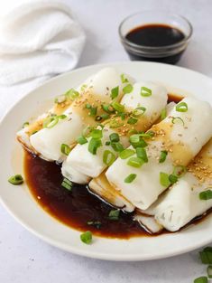 a white plate topped with dumplings covered in sauce and garnished with green onions