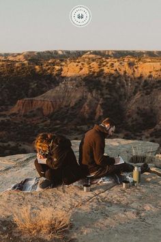 two people sitting on top of a mountain next to each other