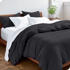 a bed with black and white comforters in a small room next to a potted plant