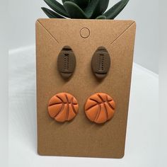 an orange pair of earrings with basketballs on them sitting in front of a plant