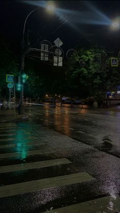 an empty city street at night with lights on and cars driving down the road in the rain