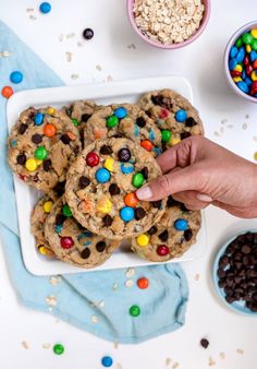 a person reaching for a cookie with m & ms on it next to bowls of cereal