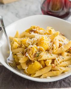 a white bowl filled with pasta and cheese on top of a table next to a glass of wine