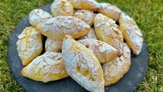 powdered sugar covered pastries on a slate platter in the middle of grass