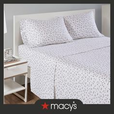 a bed with white sheets and black polka dots on it, next to a night stand