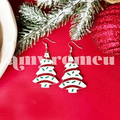 two christmas tree shaped earrings sitting on top of a red table