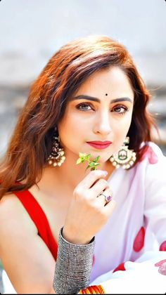 a woman with red hair and earrings is posing for the camera while holding flowers in her hand