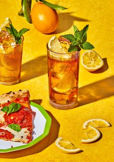 a slice of pizza on a plate next to two glasses with lemons and mint