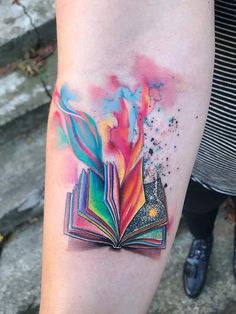 a colorful book tattoo on the left forearm and arm, with watercolors all over it