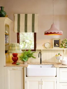 a kitchen with white cabinets and green striped curtains on the window sill above the sink